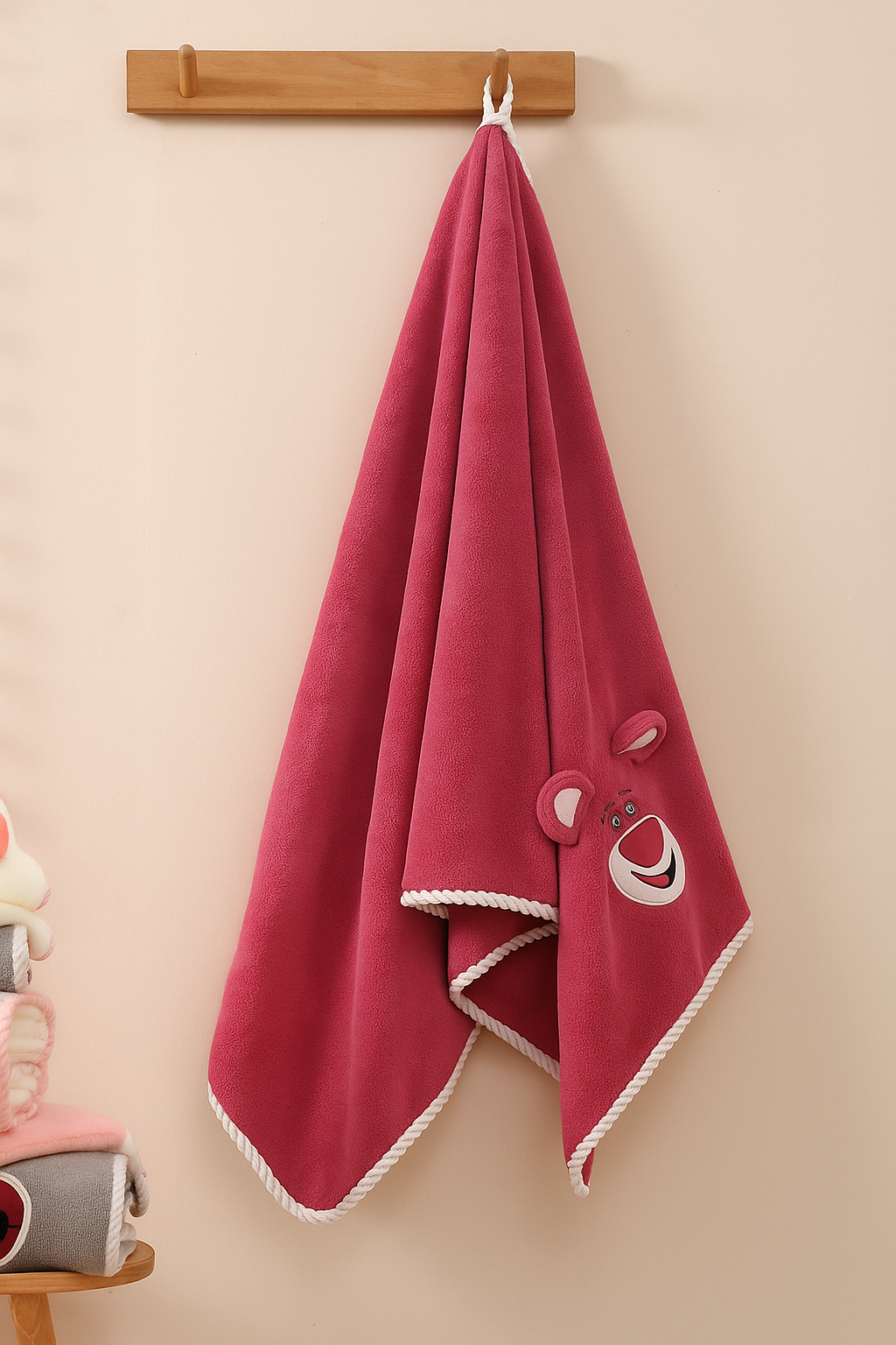 Red towel with white trim and buttons hanging on a wooden rack against a beige wall.